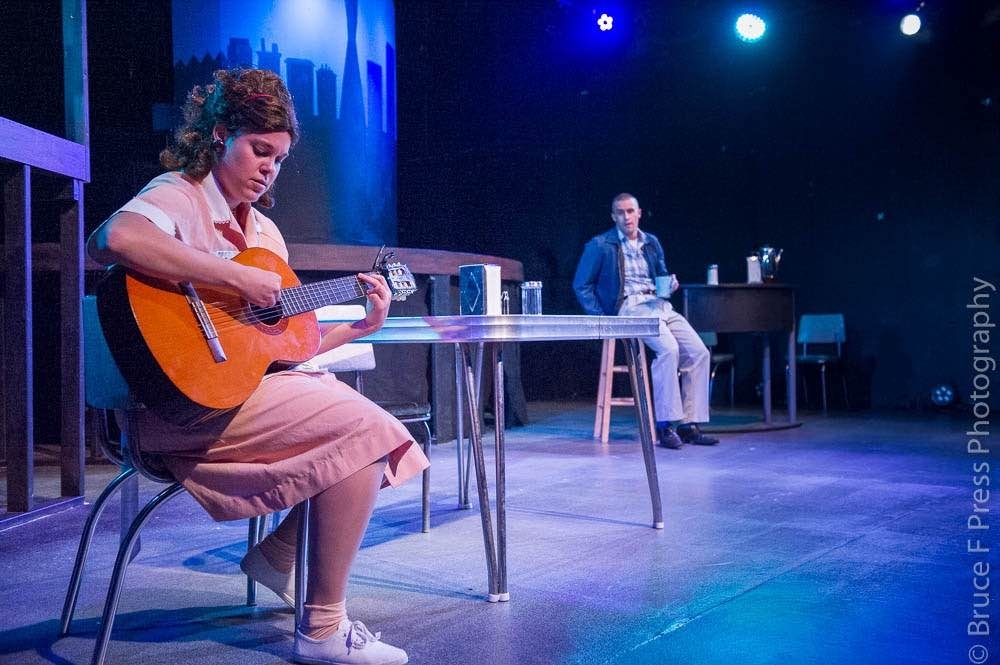 Courtney Branch as Rose strums her guitar in her mother's diner while Christian Hoff as Birdlace looks on.
