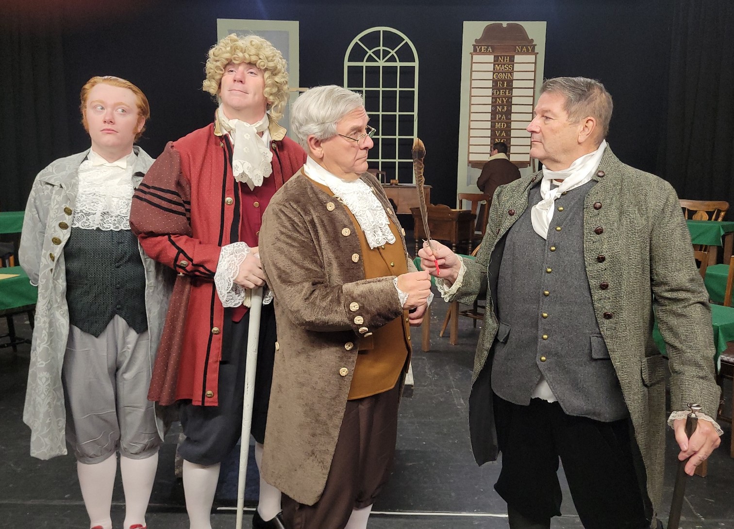 At right John Adams (Mark Dils) attempts to hand the quill pen to Ben Franklin (Roger Philippon) during the musical number But, Mr. Adams in the CLT production of 1776. Looking on from left are Thomas