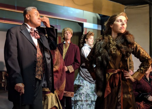 Miss Nutting, Please: Darryl Maximilian Robinson as Chairman Mr. William Cartwright/Mayor Thomas Sapsea is dismayed by Sarah Myers as Edwin Drood/Miss Alice Nutting in The Mystery of Edwin Drood.