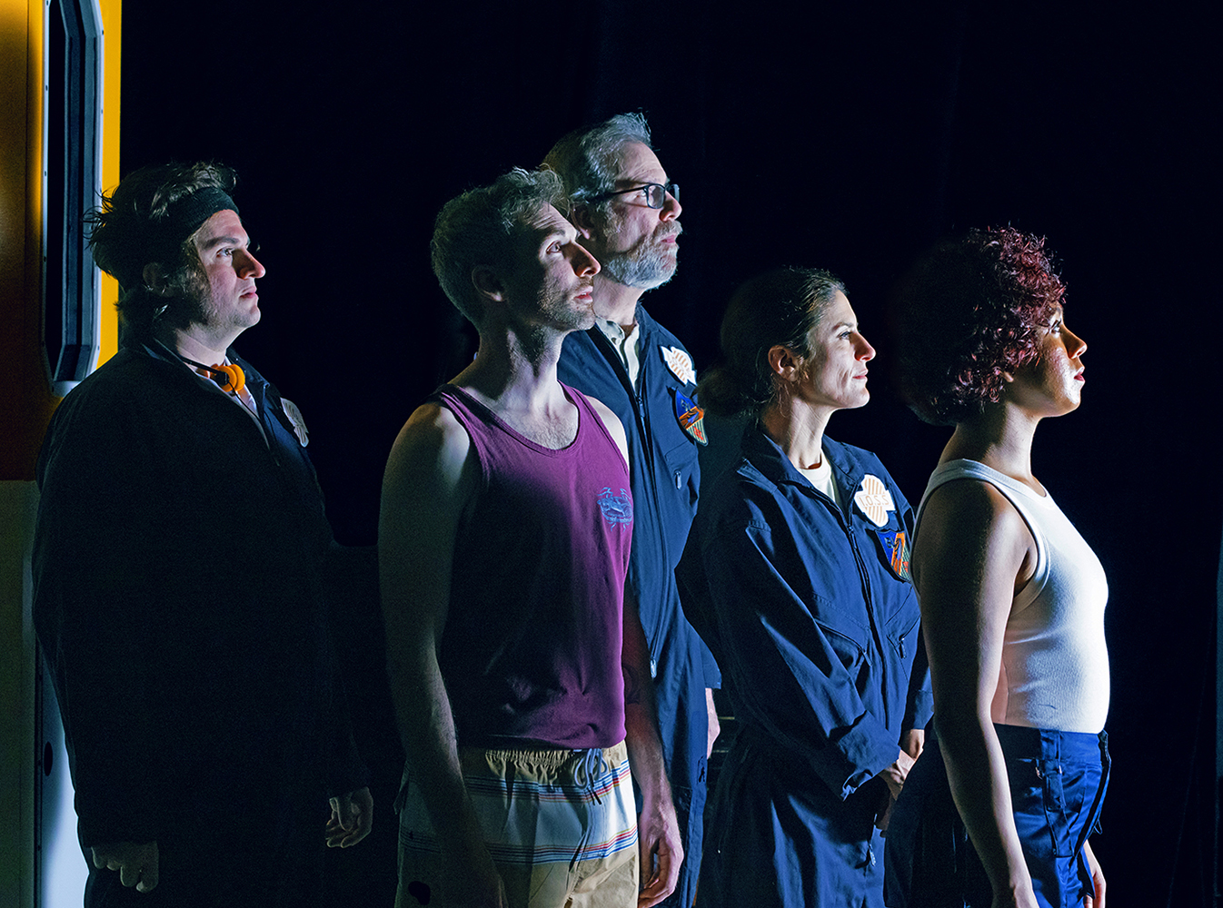 The cast of Solaris, standing in front of a black background, all in their space gear, such as dark-blue jumpsuits with the Solaris logo on the shoulder, and others are in tank tops. All of the crew of this space station are in profile to us, looking out and slightly up at... something. 