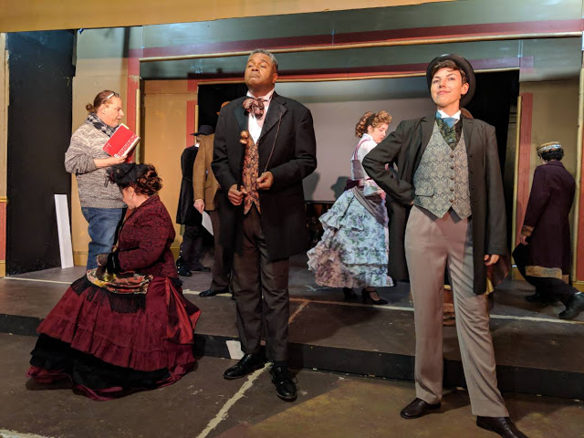 The Director of The Show Directs The Photo Shoot!: Skilled veteran director and musical director Robert-Eric West ( left with notes ) tells the show's Principal Cast ( including Darryl Maximilian Robinson as The Chairman Mr. William Cartwright at center, and Sarah Myers as Edwin Drood at right ) what he wants conveyed during the publicity photo session for the 2018 Saint Sebastian Players of Chicago Revival of Rupert Holmes' 'The Mystery of Edwin Drood'. Photo by Eryn Walanka. 