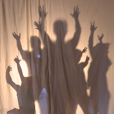 Rehearsal still: the singers in a shadow tableau in the pits of Gehenna