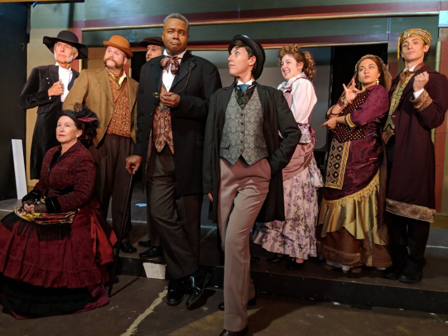 Who Would Want To Murder Such A Fine Young Man?: Surrounded by Multiple Suspects, Darryl Maximilian Robinson as The Chairman Mr. William Cartwright ( center left ) ponders who might have a reason to kill Sarah Myers as Edwin Drood ( center right ) in the 2018 Saint Sebastian Players of Chicago revival of Rupert Holmes' Tony Award-winning Best Musical Whodunit 'The Mystery of Edwin Drood'. Photo by Eryn Walanka. 