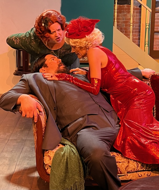 Felix Geisel (David Burkhart) is in an awkward position with Darla Chase (Elin Bhaird) on one side of him and his wife, Madge Geisel (Kristy Salisbury) on the other