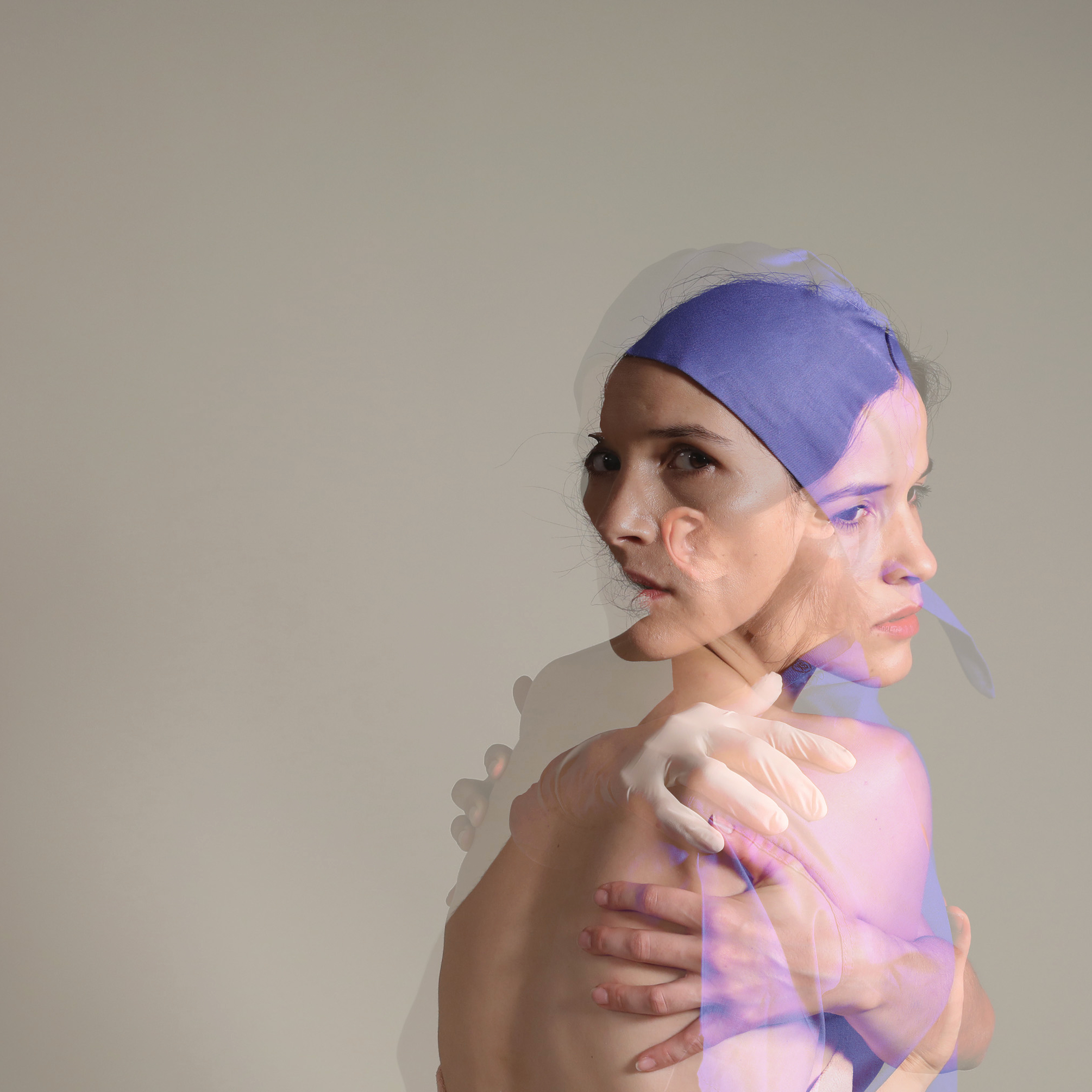 Translucent images of a white woman laid on top of each other creating a double sided person looking out to the viewer. A hand with a surgical glove is lying on the naked back of the woman.