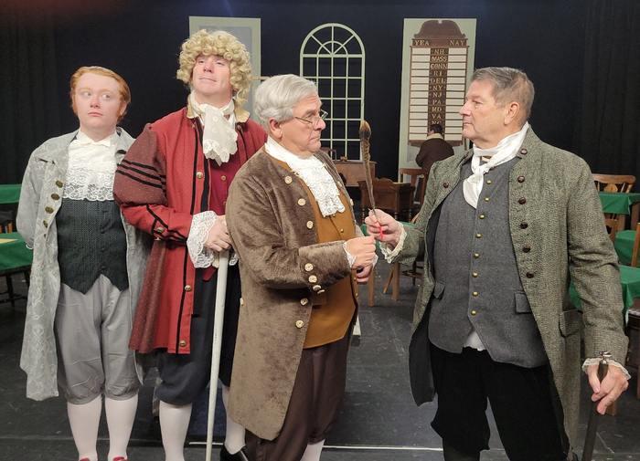 At right John Adams (Mark Dils) attempts to hand the quill pen to Ben Franklin (Roger Philippon) during the musical number But, Mr. Adams in the CLT production of 1776. Looking on from left are Thomas 1