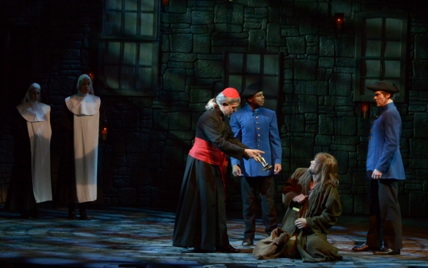 The Bishop (Gabriel Zenone) offers a gift to Valjean (Gregg Goodbrod), seated, as the Photo