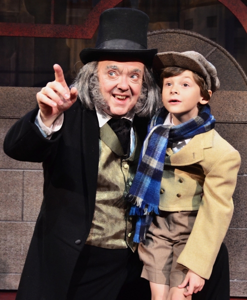 A newly-reformed Ebenezer Scrooge (Eddie Curry) celebrates Christmas with Tiny Tim (H Photo
