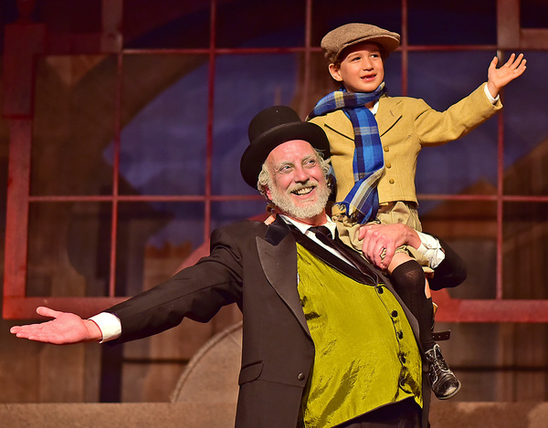 Ebenezer Scrooge (Jeff Stockberger) lifts Tiny Tim (Ashton Curry) Photo