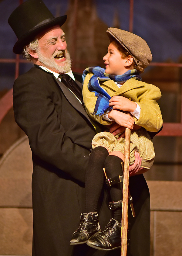 Ebenezer Scrooge (Jeff Stockberger) lifts Tiny Tim (Ashton Curry) Photo