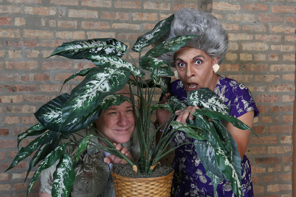 Chester Nurdiger (Ed Jones) and Mother Nurdiger (David Cerda) hide behind a plant in  Photo