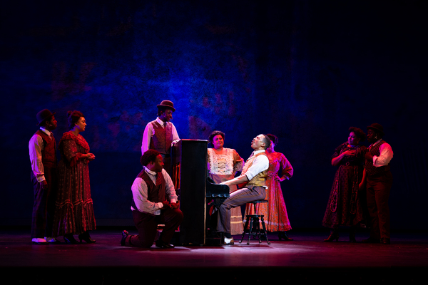 Charl Brown as Coalhouse Walker Jr. (center at piano) with members of the company Photo