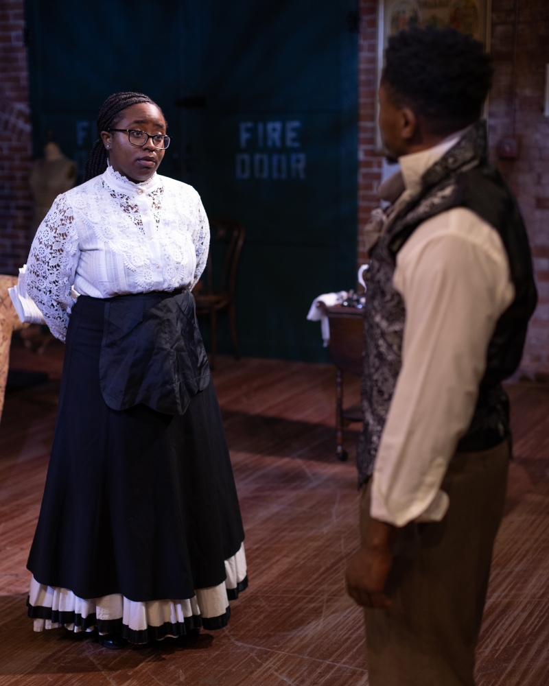 Connie, a young Black woman in a 19th-century maid uniform, looks at Ira Aldridge, a young Black actor