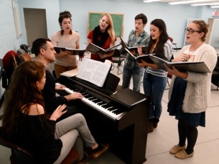  Zoe Sarnak seated at piano, with Robert Meffe (playing). Gathered around the piano,  Photo