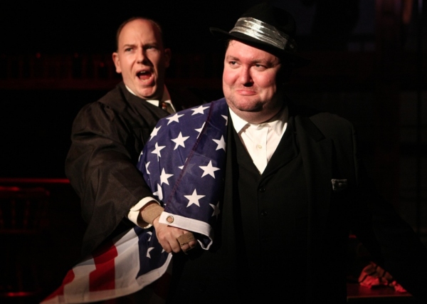 J. Edgar Hoover (E.J. Subkoviak) is wrapped in an American flag by the narrator (Jake Photo